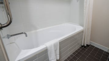 A standard white bathtub with a shower head, a towel hanging on the side, and a tiled floor.