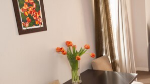 Een eettafel met een vaas tulpen, een lijst met een schilderij en uitzicht op een gordijn.
