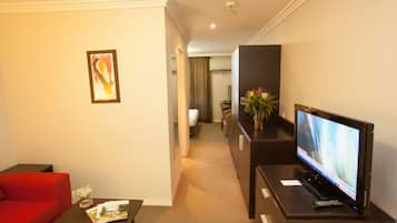 Quarto de hotel com televisão, sofá vermelho, uma mesinha com um vaso e um quadro na parede.