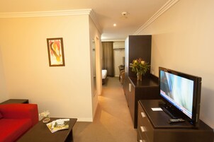 Una habitación de hotel con televisión, un sofá rojo, una mesita con un jarrón y un cuadro en la pared.