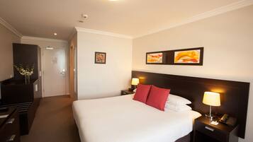 Een hotelkamer met een groot bed, twee nachtkastjes met lampen, een bureau met stoel en een dressoir.