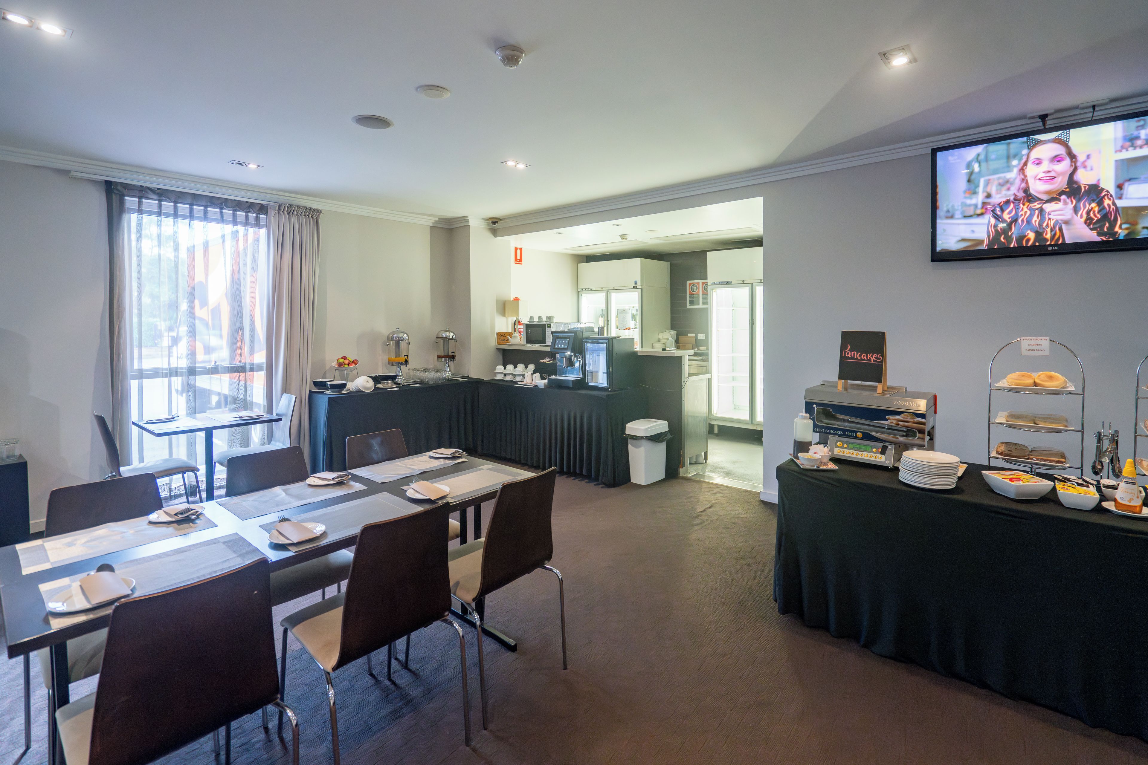 Une salle de conférence avec une longue table préparée pour une réunion, un écran de télévision et un espace buffet proposant divers plats.