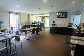A hotel dining area with tables and chairs, a kitchen in the background, and a television on the wall. - Wine Country Motor Inn (Cessnock)