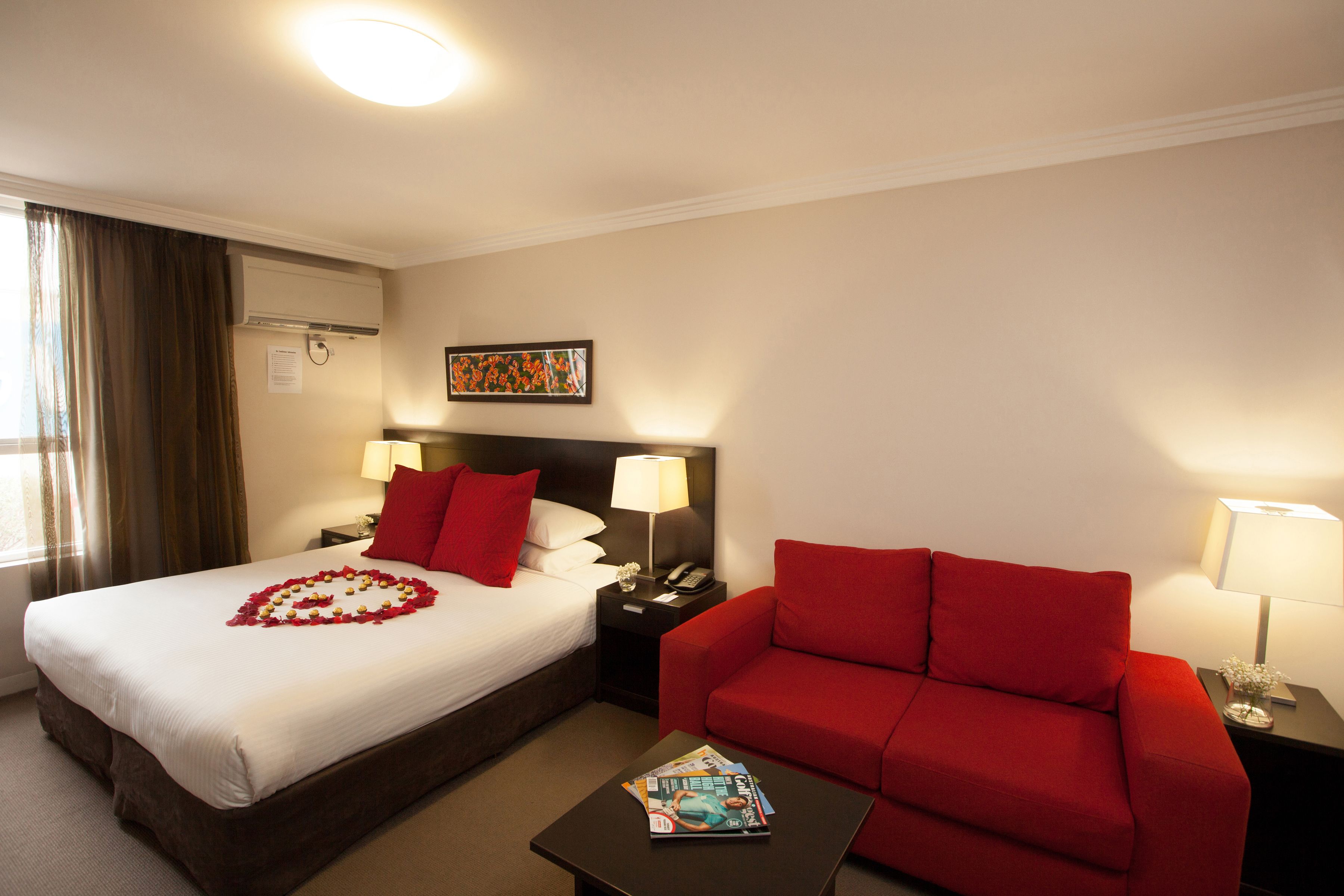 Ein Hotelzimmer mit einem Bett, einem roten Sofa, einem kleinen Tisch mit einer Zeitschrift und einem Nachttisch mit einer Lampe.