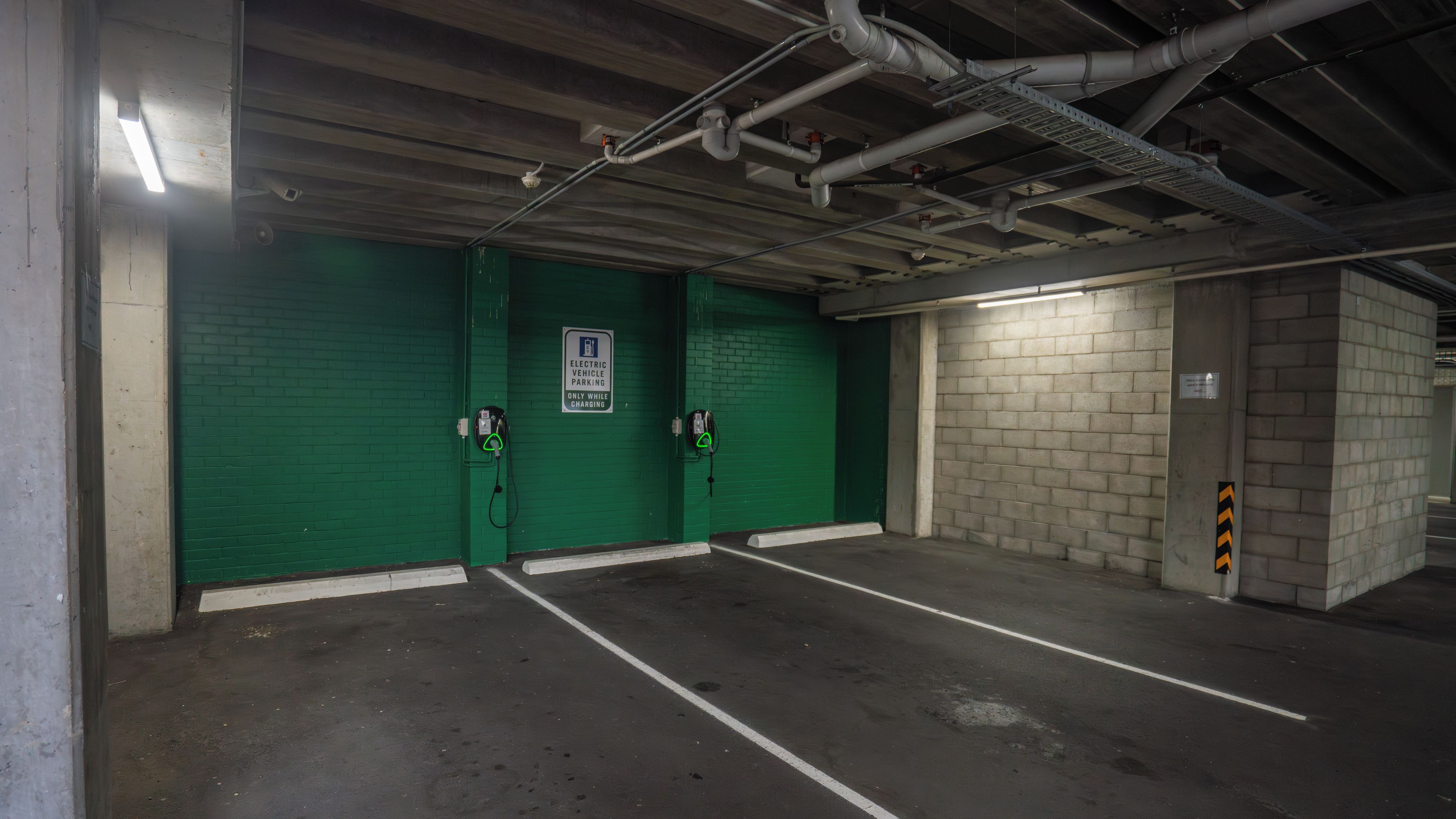 An underground parking garage with green walls, two electric vehicle charging stations, and a concrete pillar with a caution sign.