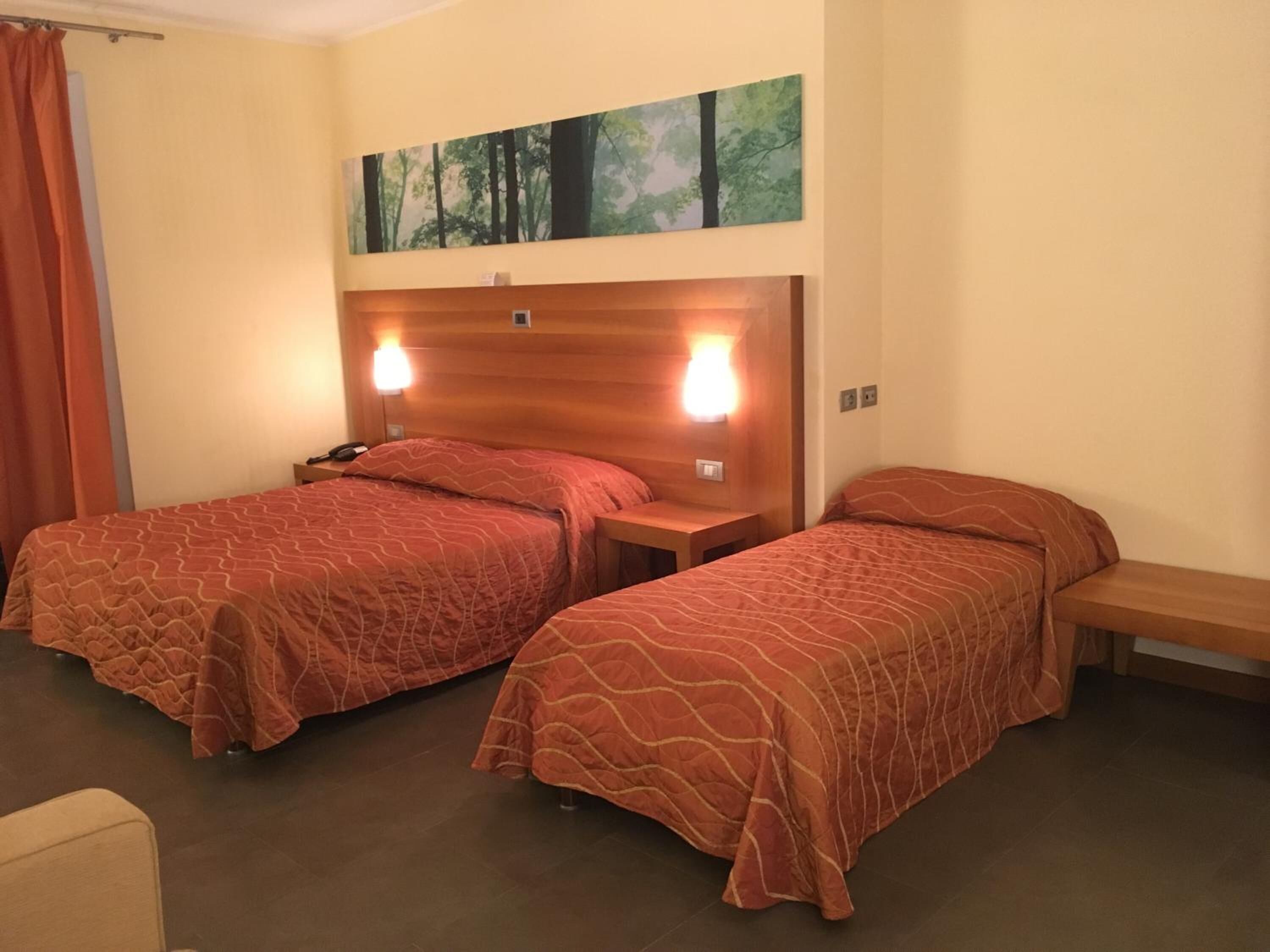 Camera d'albergo con due letti, una testiera in legno, un quadro sopra i letti e una panca.