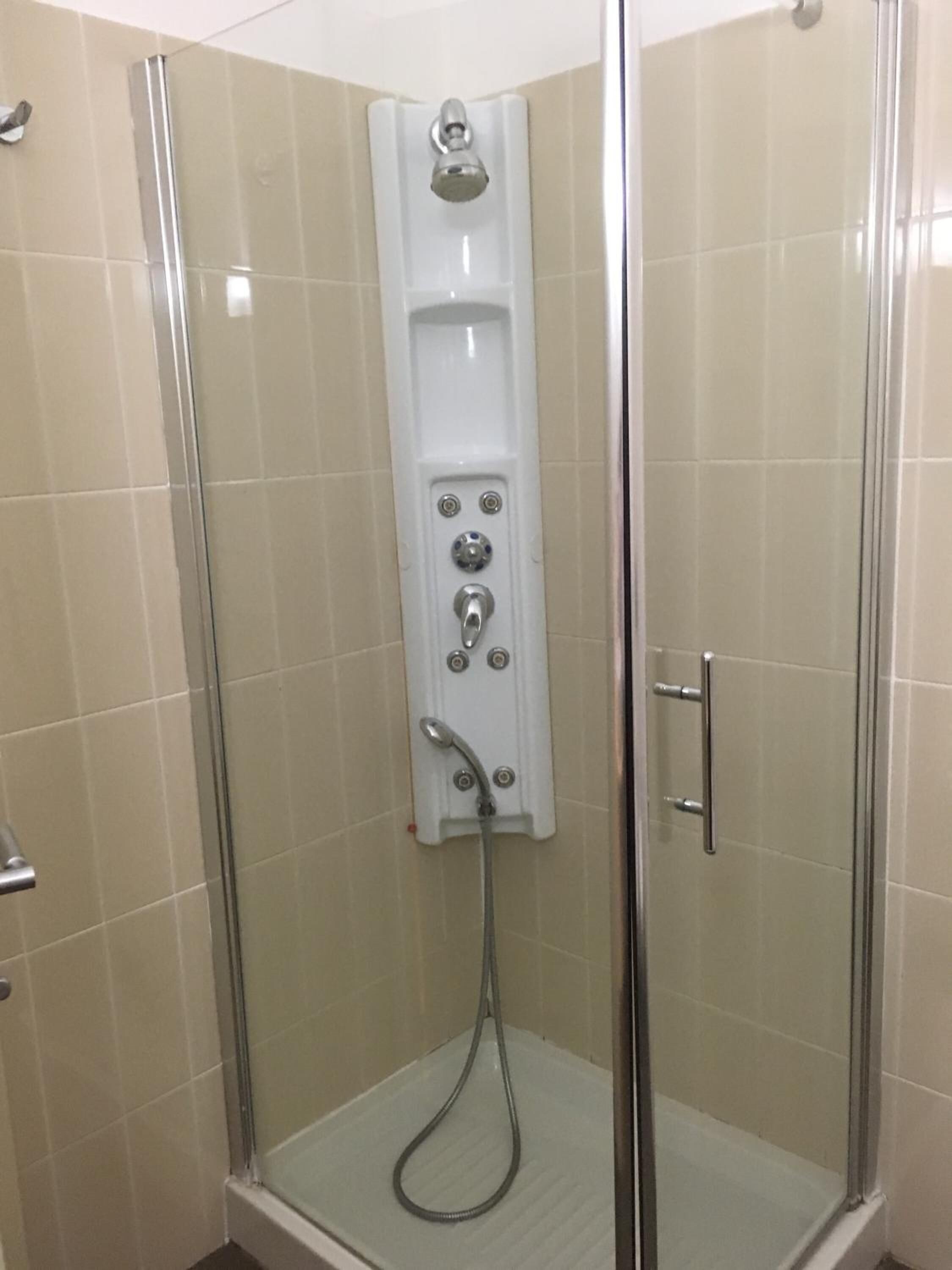 A glass-enclosed shower stall with a control panel for water temperature and flow, a handheld showerhead, and a glass door.