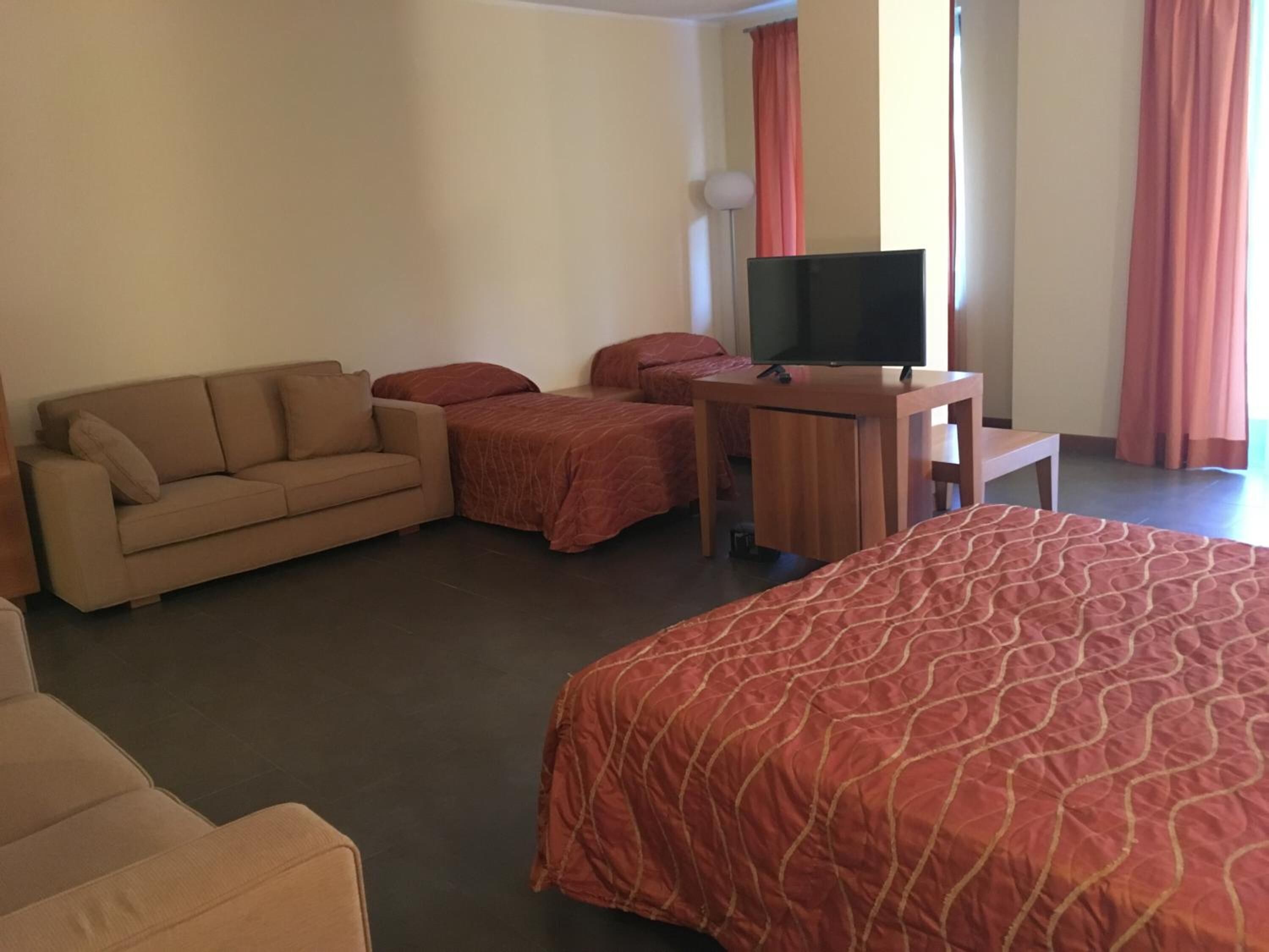 Ein Hotelzimmer mit einem großen Bett, einer Couch, einem Schreibtisch mit Fernseher und einem Sessel.