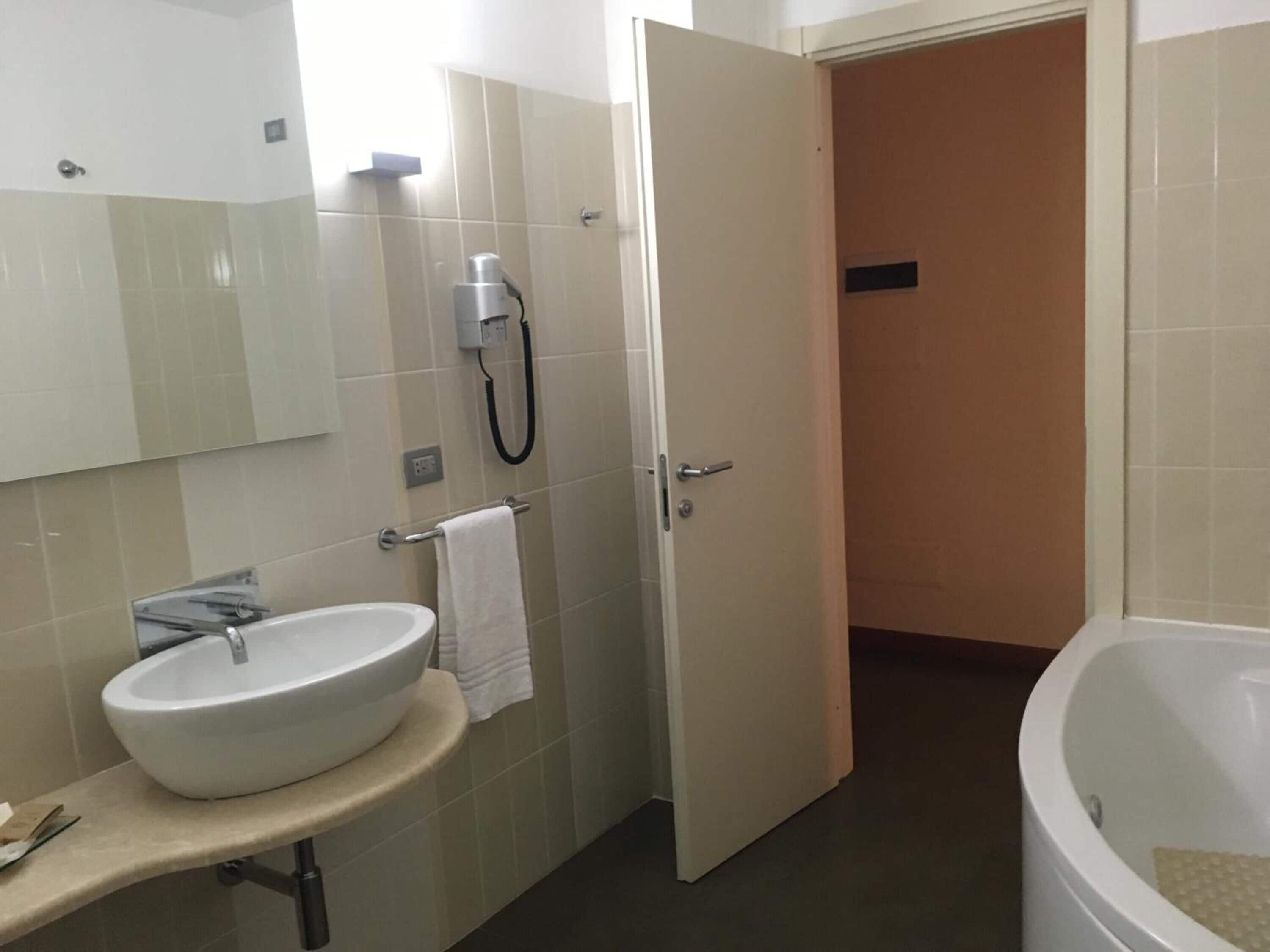 Un baño con lavamanos blanco, espejo, toallero y zona de ducha.