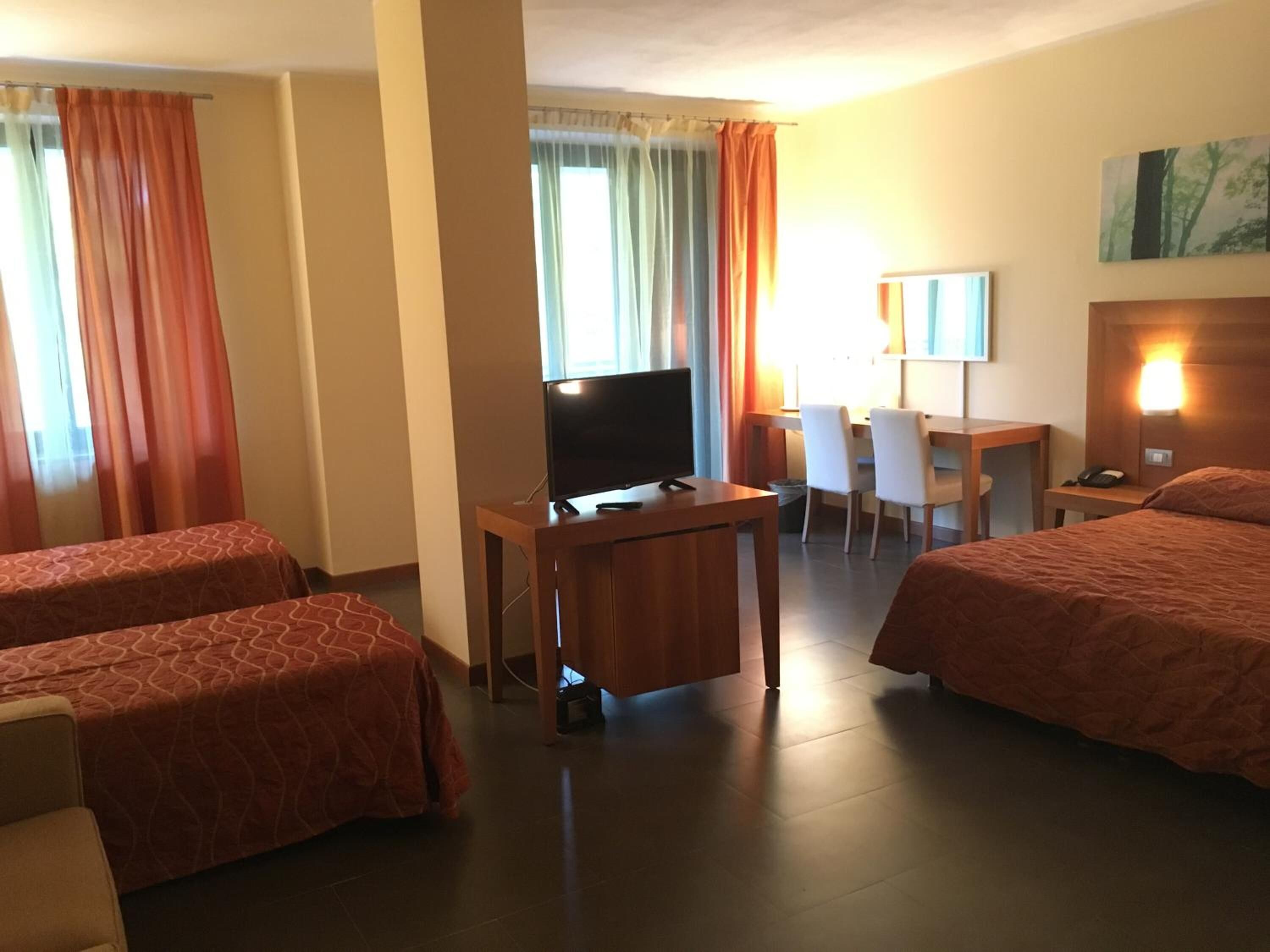 Ein Hotelzimmer mit zwei Betten, einem Schreibtisch, einem Fernseher und einem Sessel.