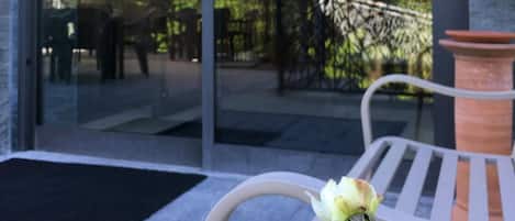 The entrance of Hotel Langhe & Monferrato with a glass door, outdoor seating area, and a white chair with a single rose.