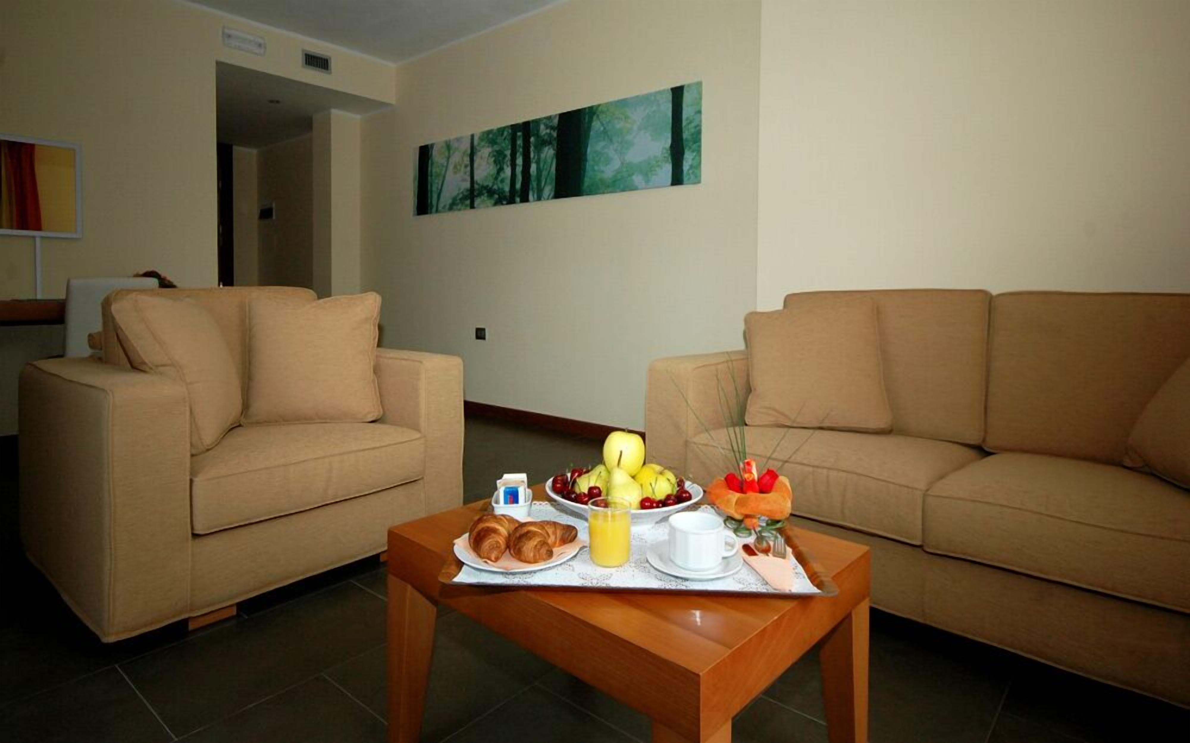 A living room with two beige sofas, a wooden coffee table with breakfast items, and a painting on the wall.