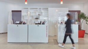 Un espace d’accueil comprenant deux comptoirs de réception blancs, un terminal d’enregistrement numérique et une plante en pot.