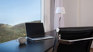 Un ordinateur portable est posé sur un bureau, à côté d’une tasse, d’une lampe et d’une chaise, avec vue sur un paysage vallonné.