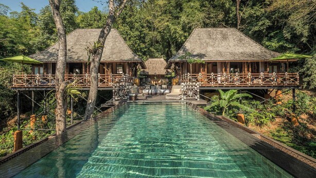 Resort com piscina, estruturas de madeira e vegetação exuberante.