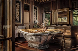A luxurious bathroom with a large freestanding bathtub, ornate wall decorations, and a large mirror.