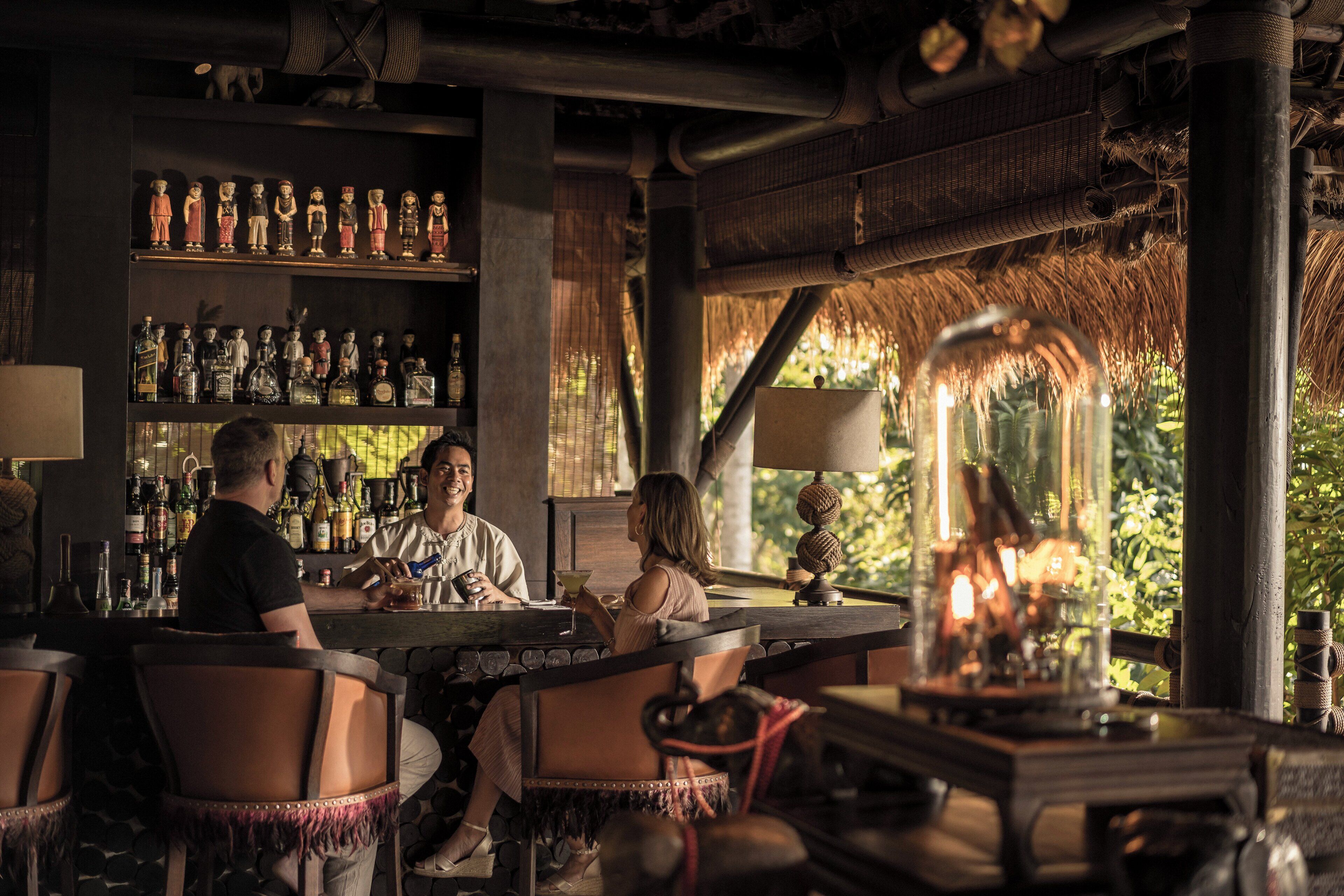 Zona de bar con muebles de madera, varios botellones en estanterías y vistas al exterior con vegetación.