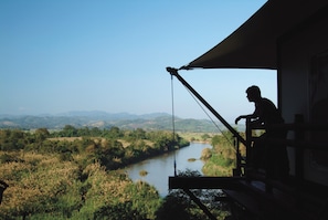 A person fishing from a balcony overlooking a river and hills.