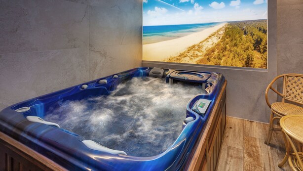 A spa area with a hot tub, a beach view poster, and a wicker chair.