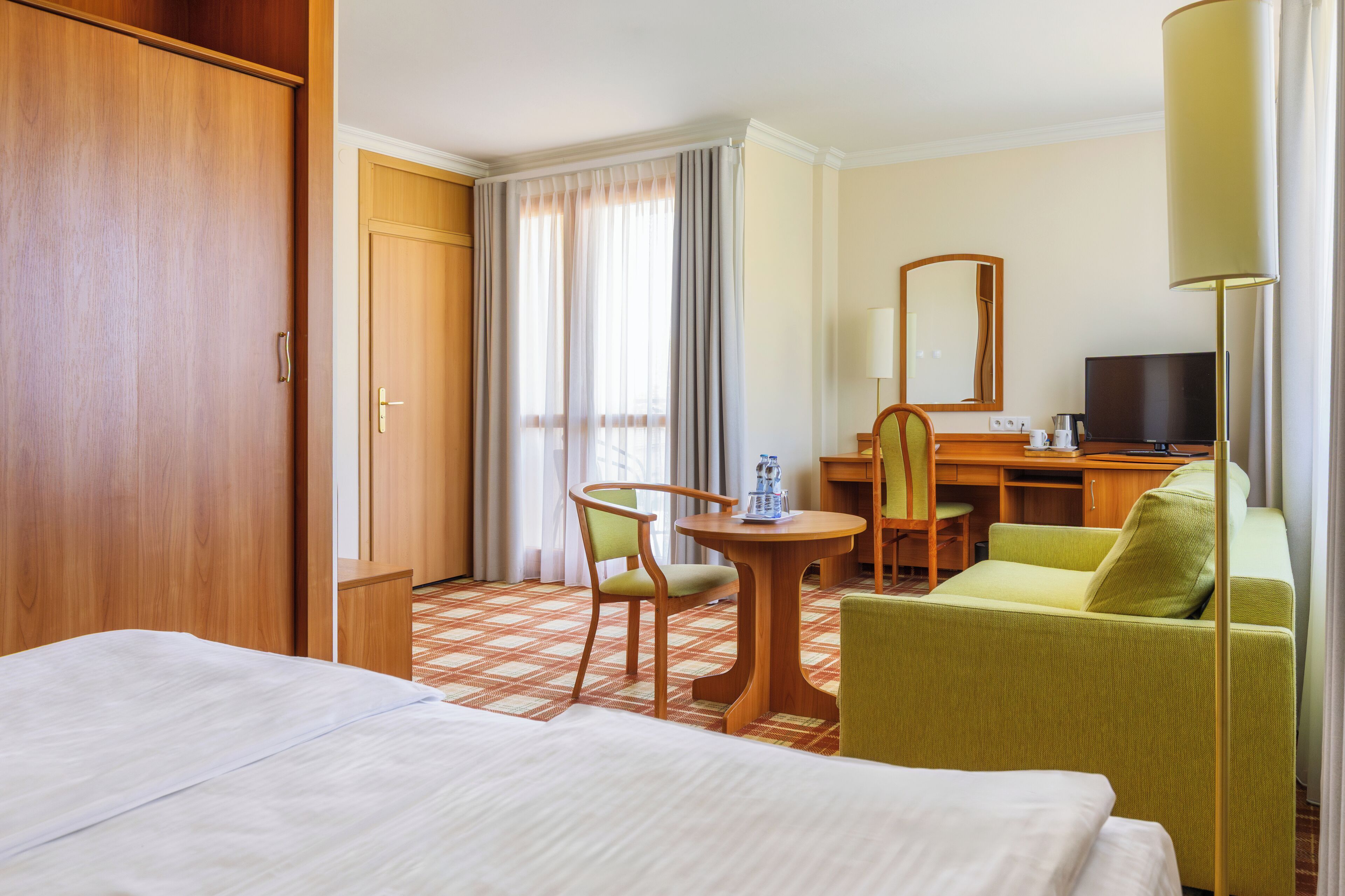 A hotel room with a bed, a desk with a chair, a sofa, a television, and a lamp.