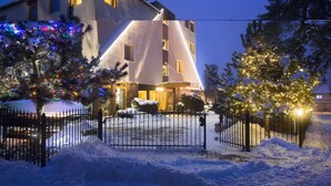 A hotel with a modern design, featuring a snow-covered entrance and illuminated trees.