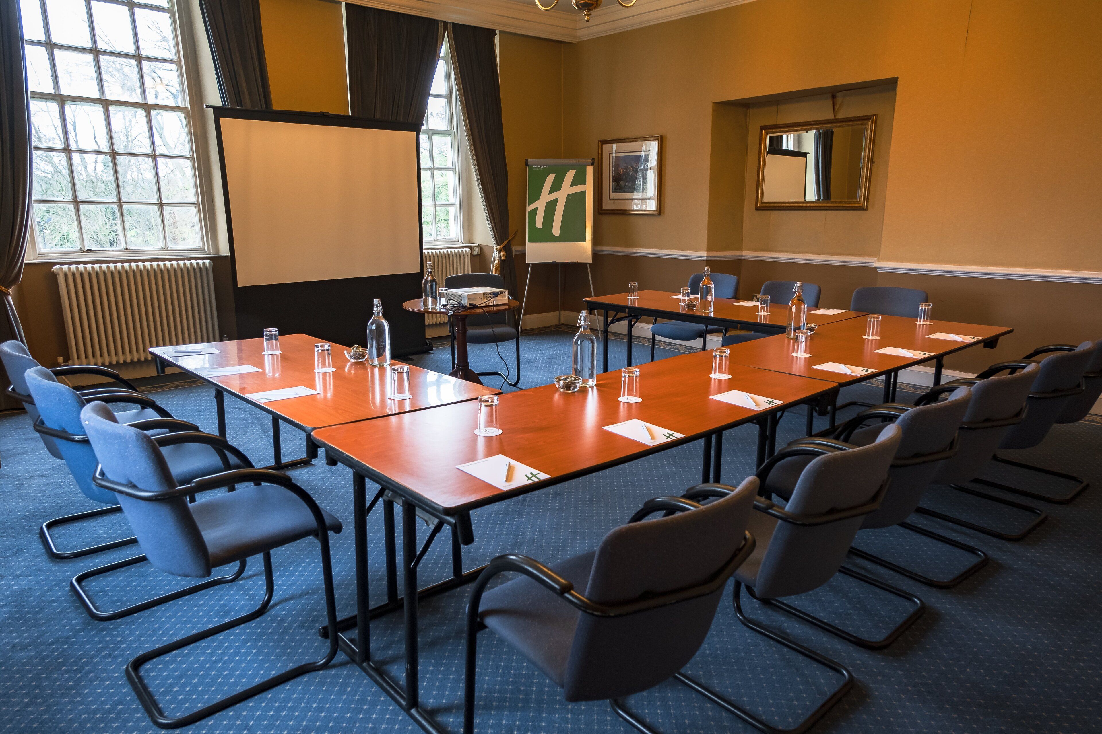 Un salón de conferencias con una larga mesa, sillas, una pantalla de proyector y una pizarra.