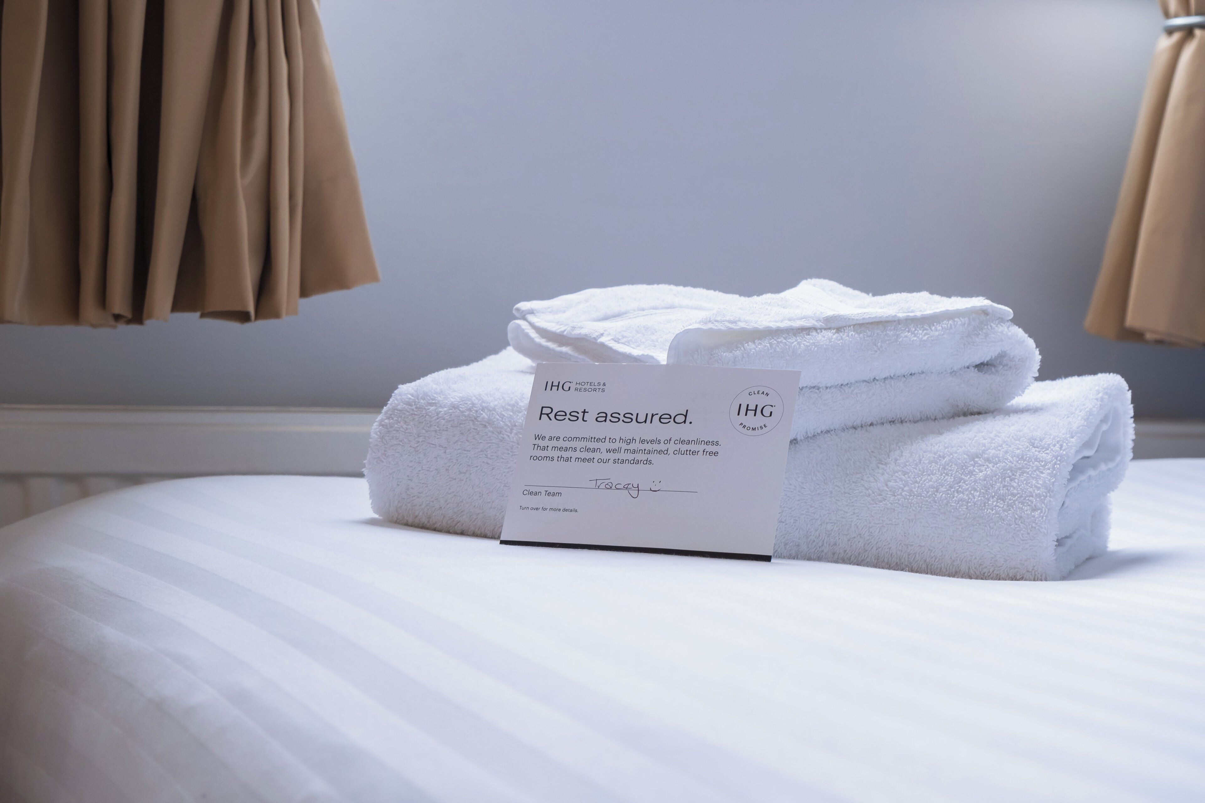 A neatly made bed with a folded white towel and a tag stating 'Rest assured.'