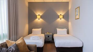 A hotel room with two beds, a sofa, and a nightstand with a lamp.