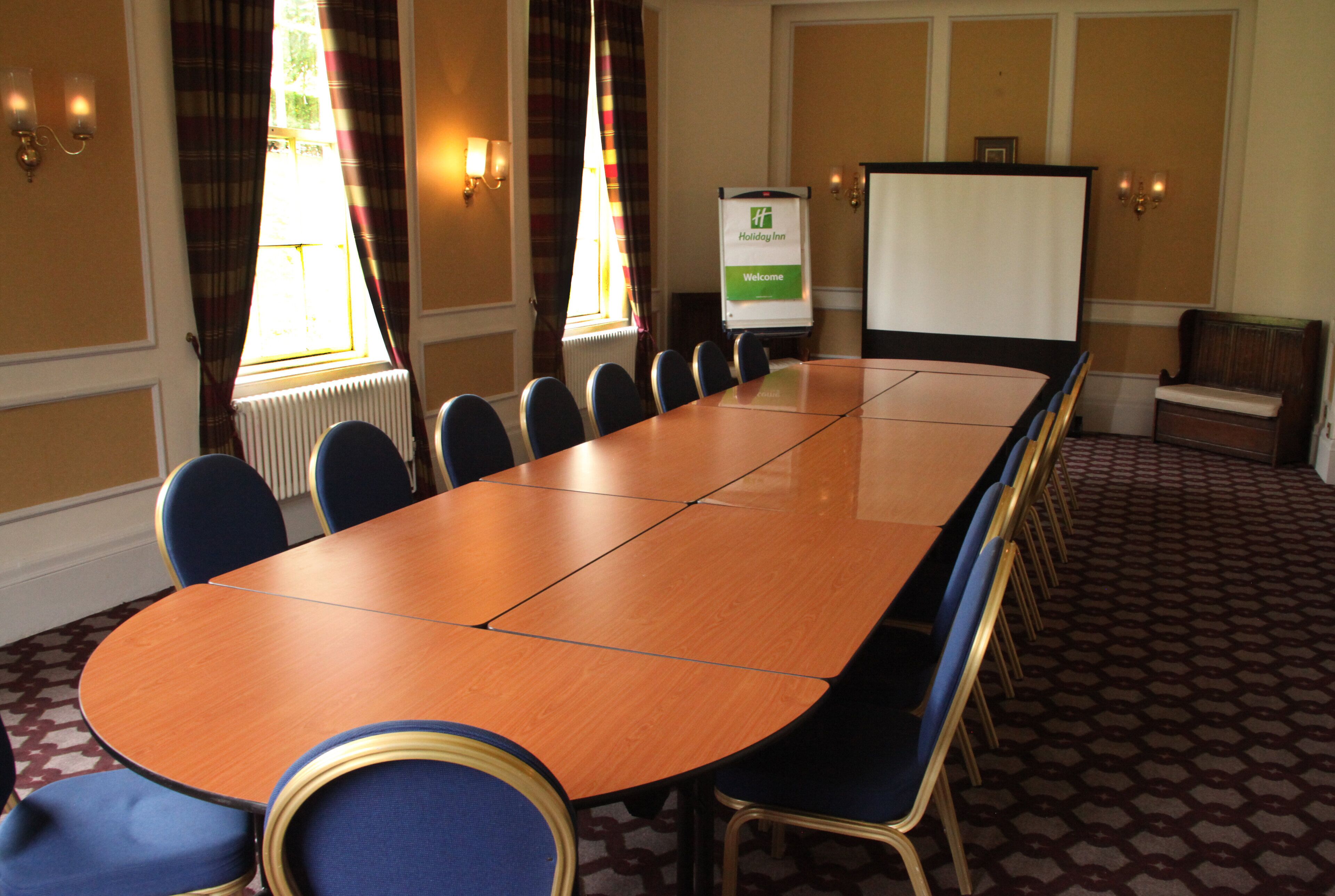A conference room with a long table, chairs, a whiteboard, and a sign reading "Holiday Inn Welcome".