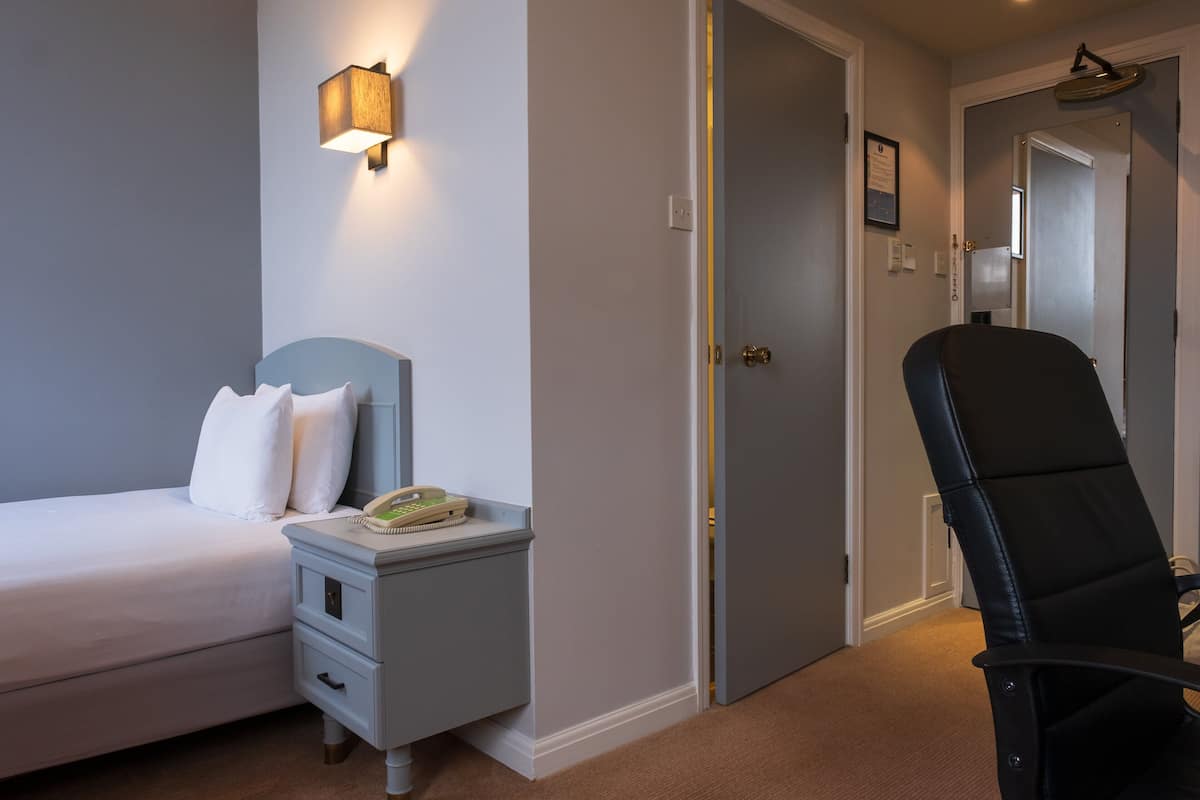 A bedroom with a bed, bedside table, lamp, and a chair.