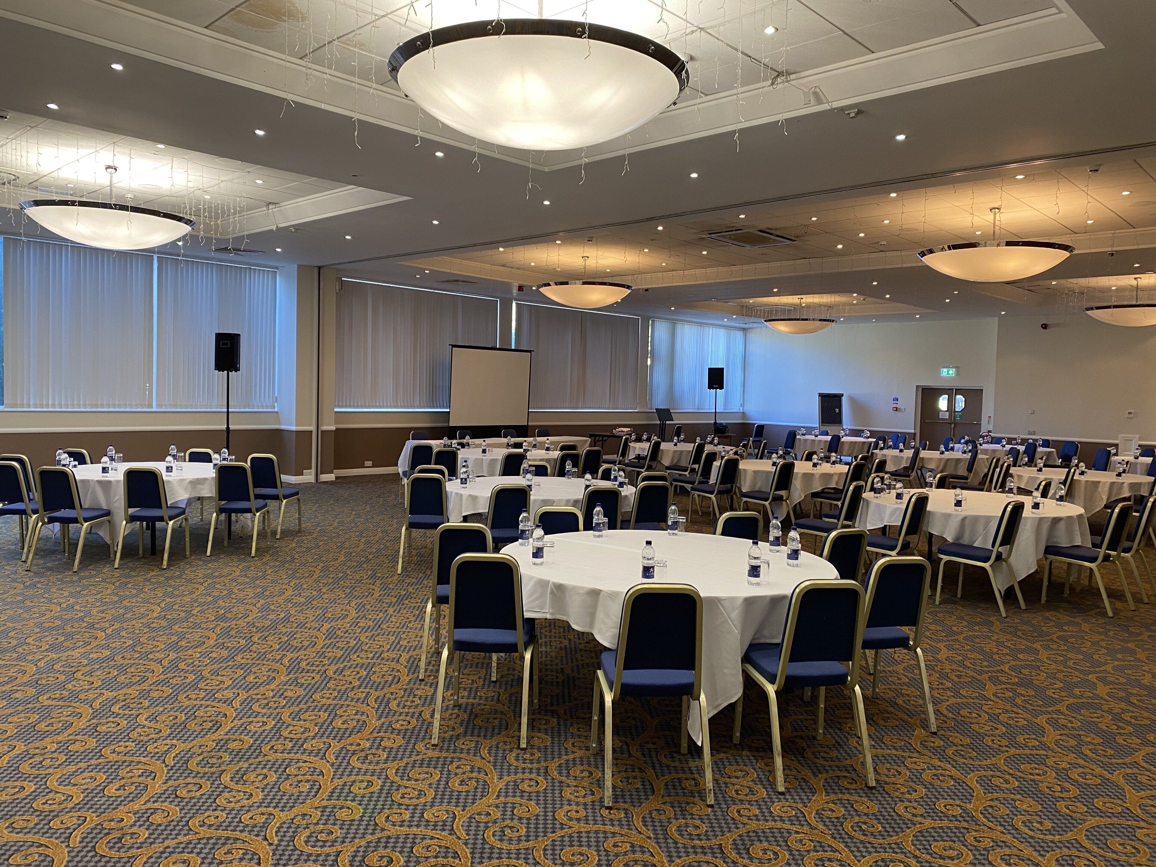 A conference room with round tables, chairs, and a projector screen.