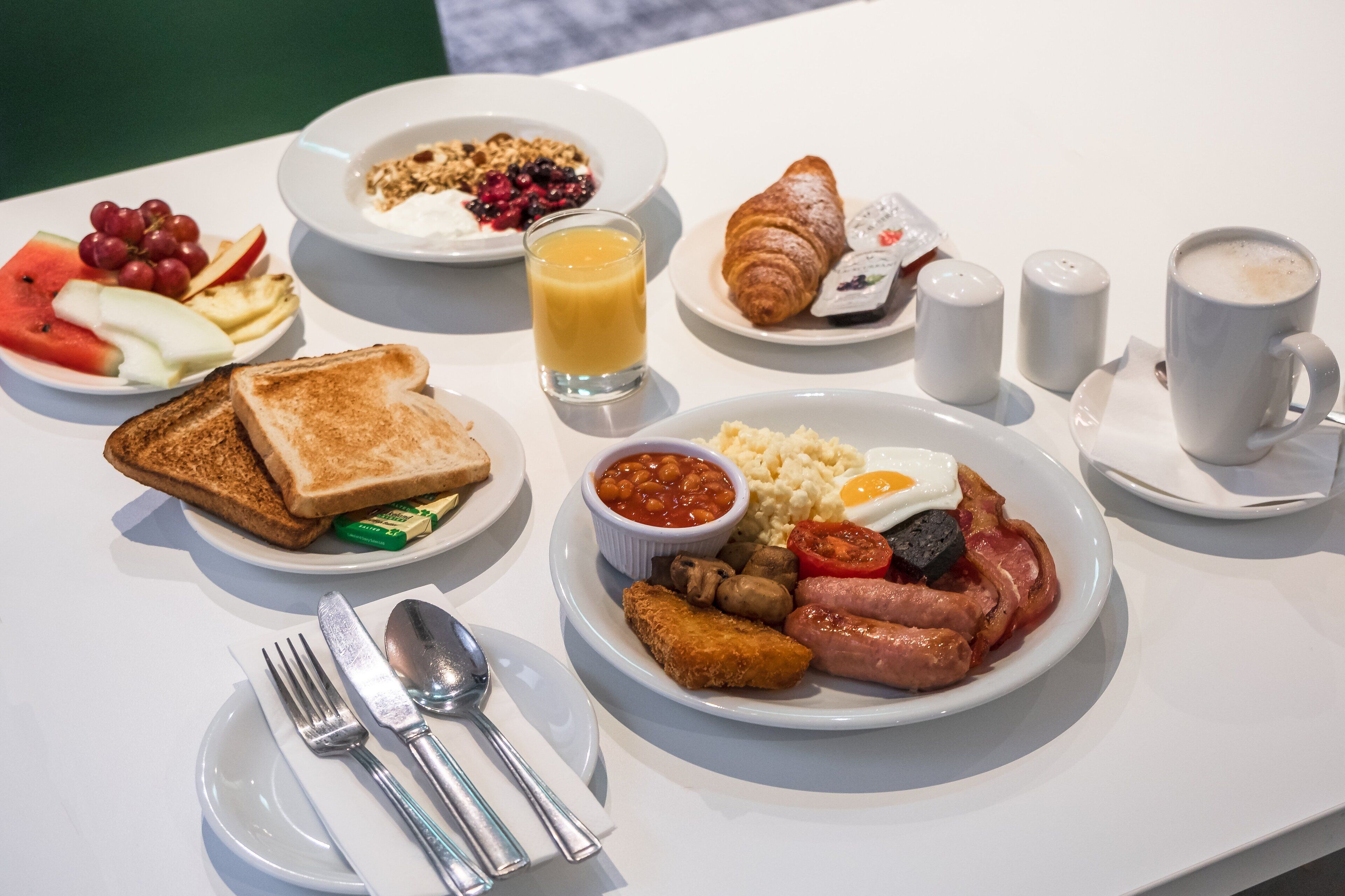 Una mesa de desayuno con tostadas, mermelada, huevos, salchichas y un croissant.