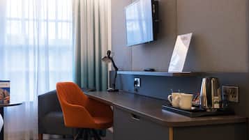 Una habitación de hotel con escritorio, una silla, televisor montado en la pared y ventana con cortinas.