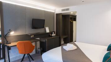 A modern hotel room with a desk, chair, bed, TV, and a walk-in closet.