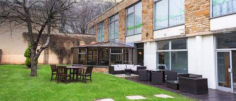 A modern building with a patio area featuring outdoor furniture and a glass enclosure.