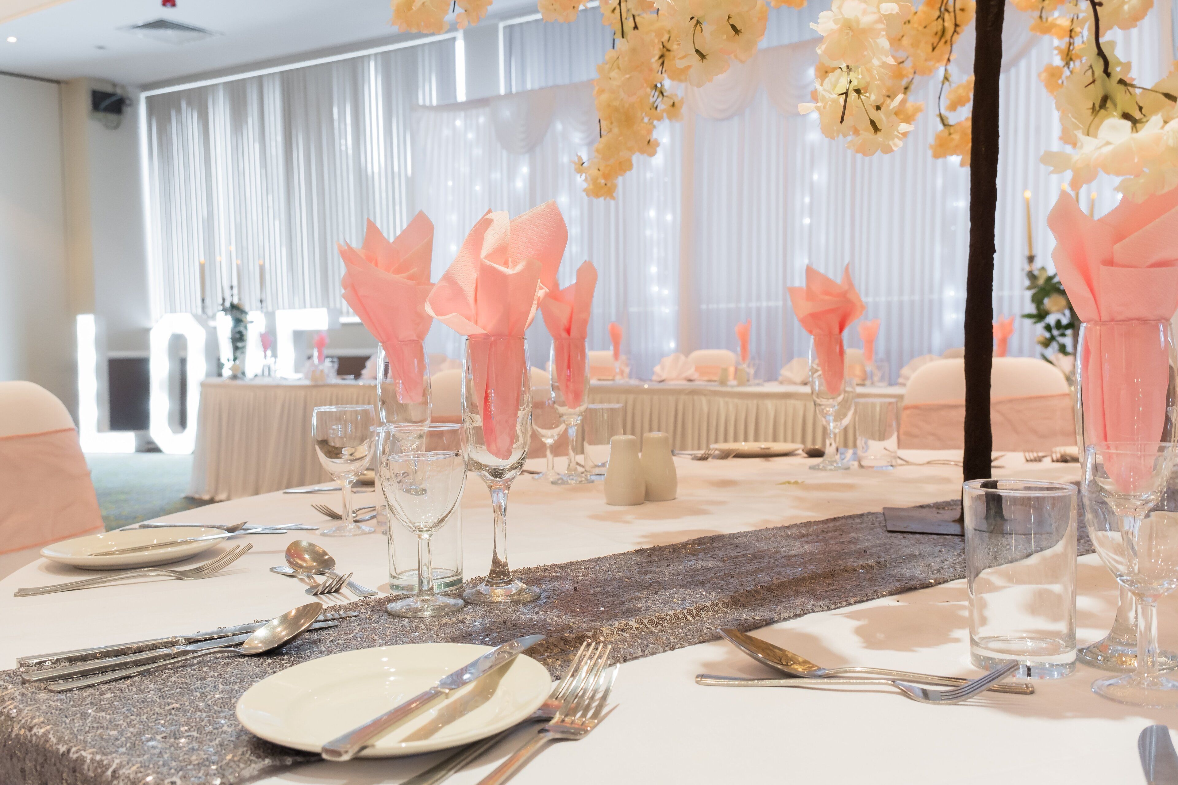 A table set for a formal event with white tablecloths, pink napkins, and clear glassware.