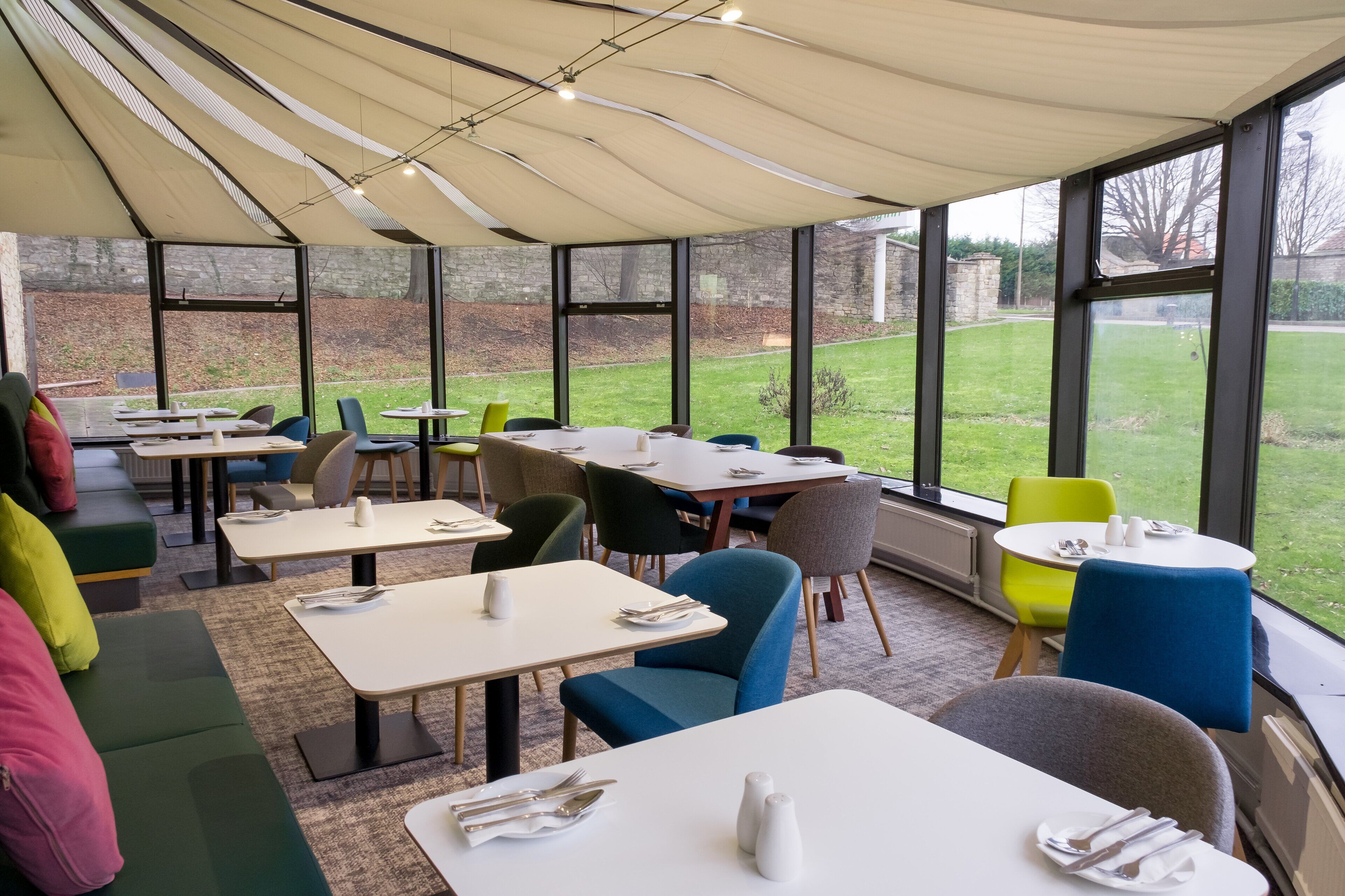 Een overdekt terras met eettafels en stoelen, grote ramen en uitzicht op de tuin.