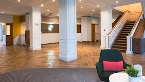 A spacious lobby with a wooden floor, white columns, a staircase, and a green armchair with a red pillow. - Holiday Inn Doncaster A1 M Jct 36 by IHG (Doncaster)