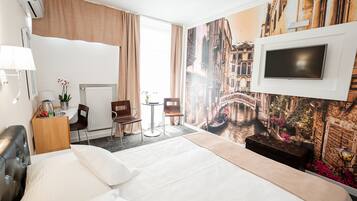 Una camera d'albergo con un letto, una scrivania, sedie, una televisione e un affresco raffigurante un paesaggio urbano.