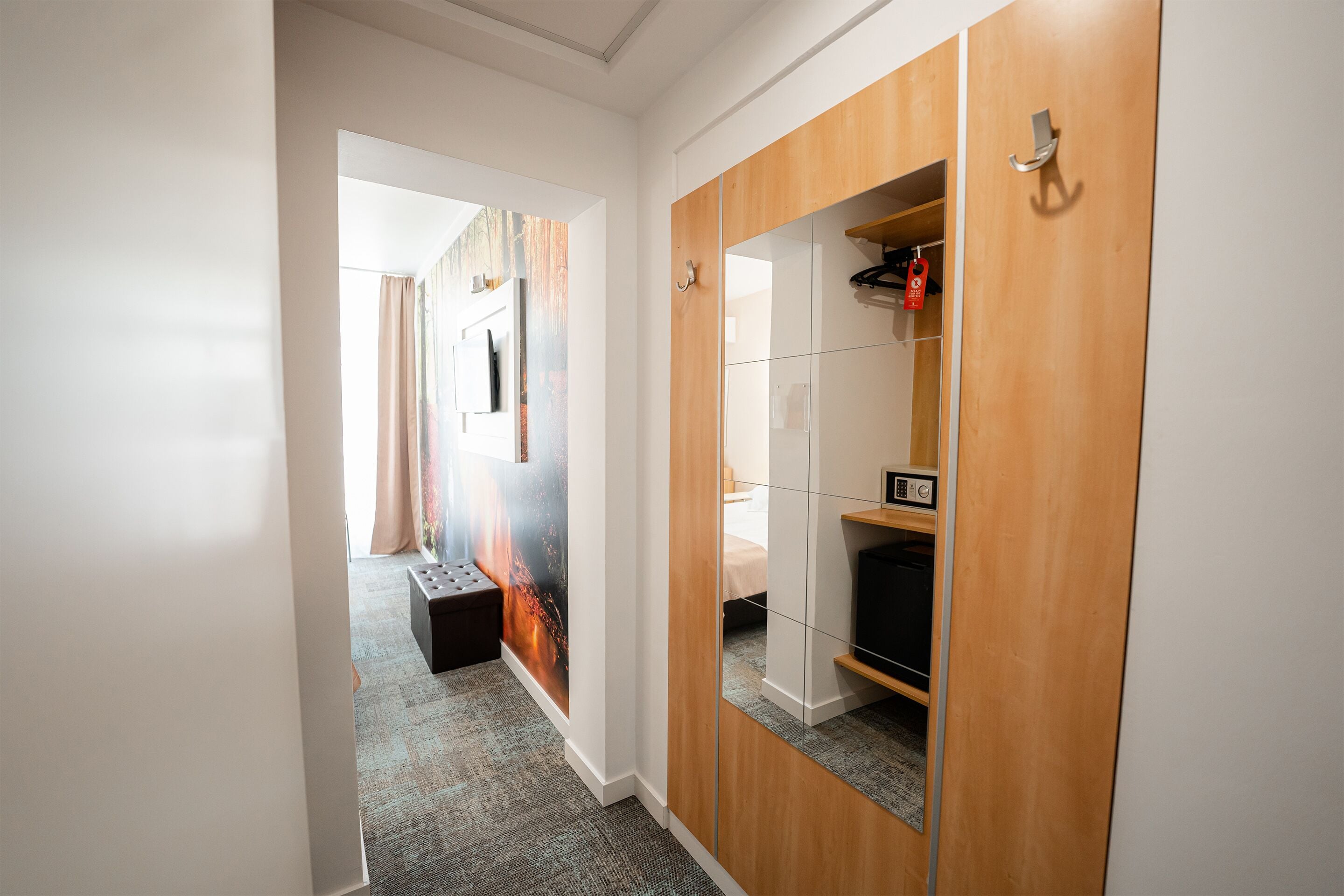 A hallway with a mirrored wardrobe, a small seating area, and a television.