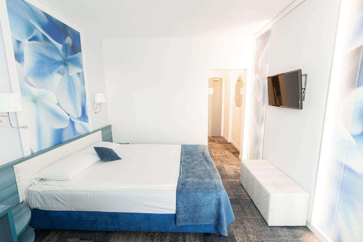A hotel room with a bed, a TV mounted on the wall, and a bench.