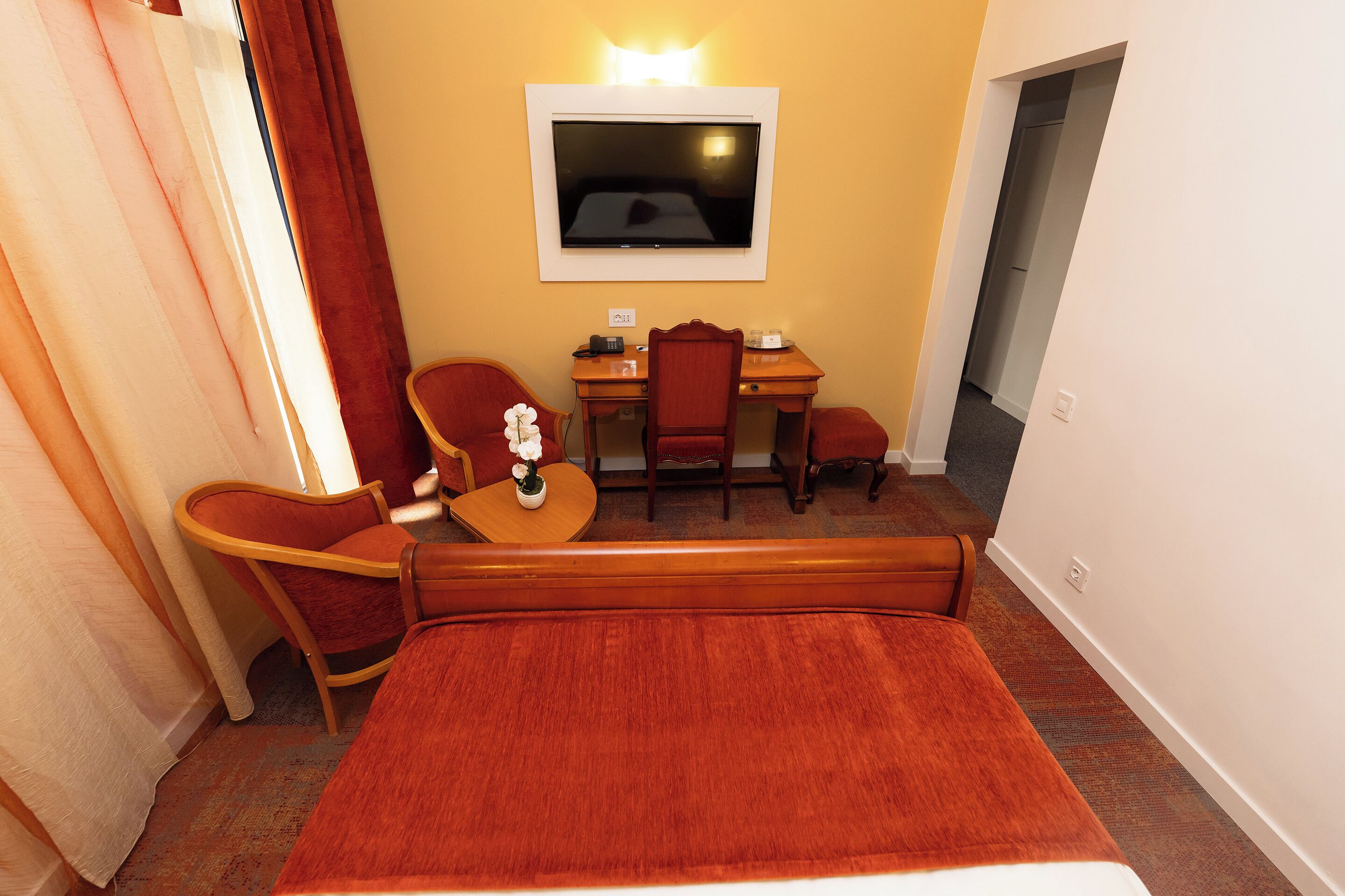 A hotel room with a bed, a desk, two chairs, a TV, and a small table with a vase.