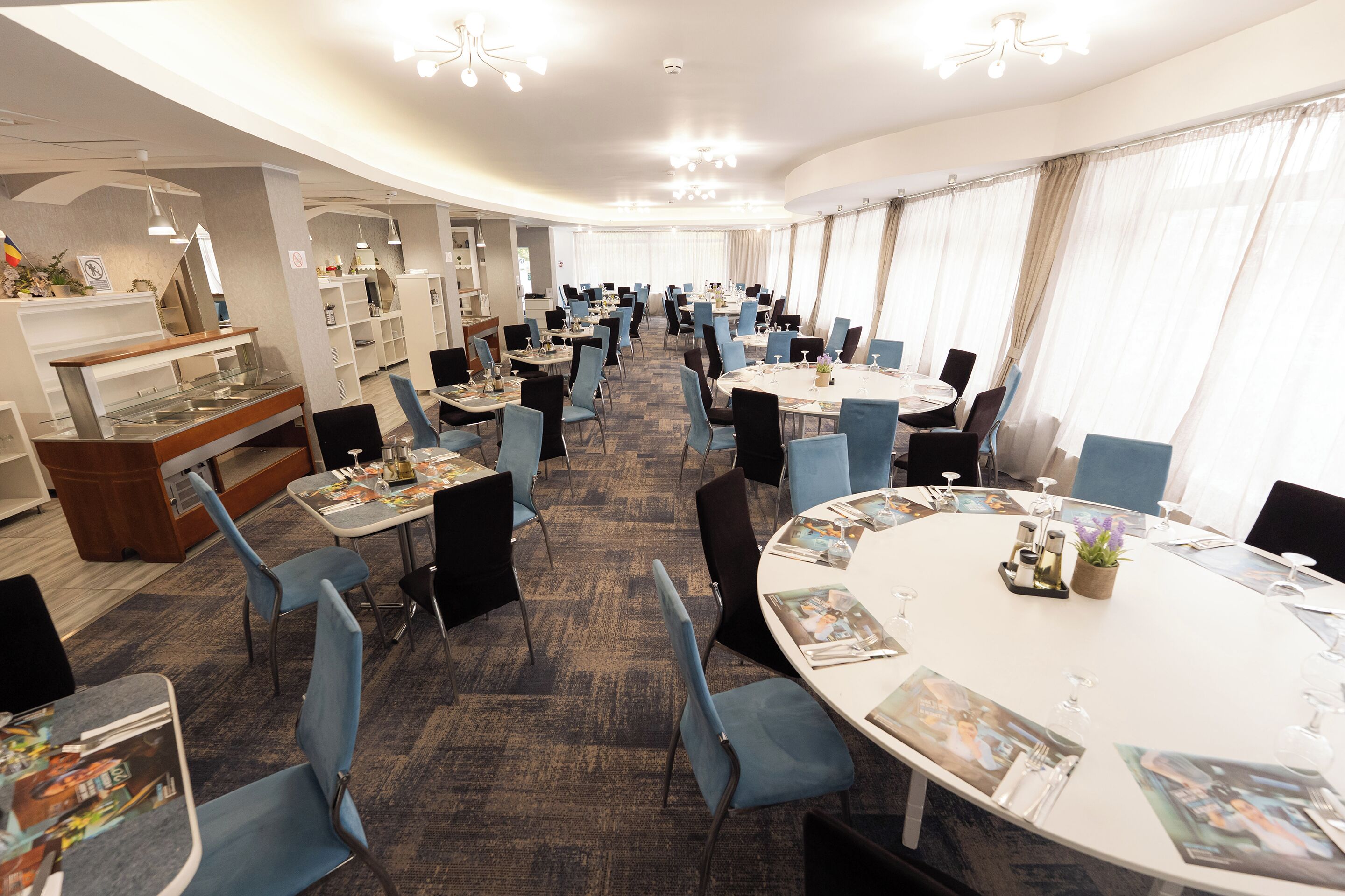 A hotel conference room with round tables, blue chairs, and a carpeted floor.