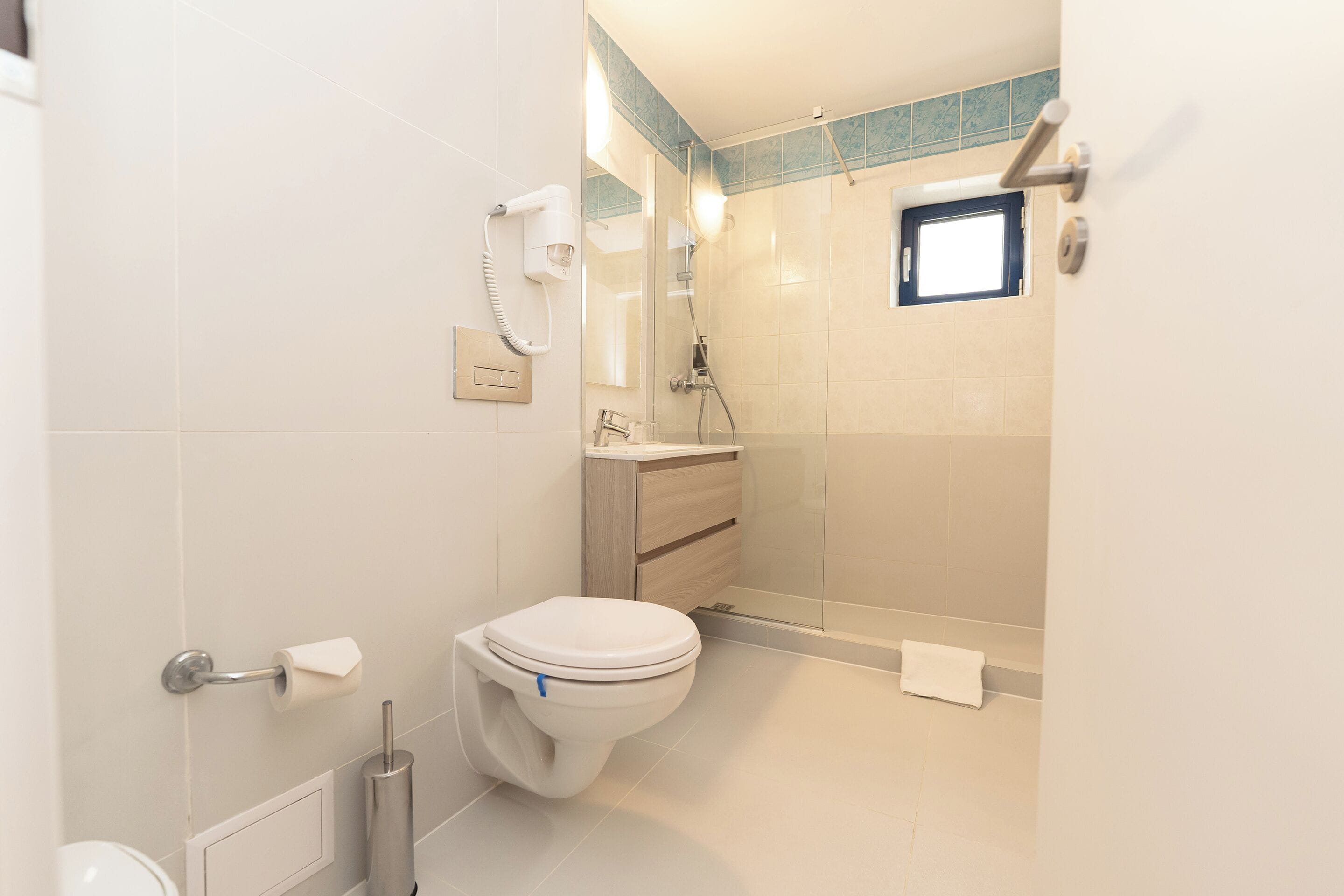 Et moderne badeværelse med toilet, håndtørrer, håndklædeholder og bruseområde.