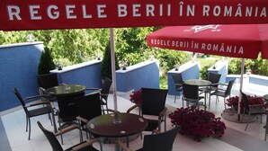 An outdoor seating area with tables and chairs, a red umbrella, and potted plants. - MyContinental Suceava (Suceava)