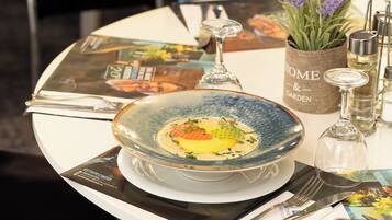 A dining table with a blue ceramic bowl containing a dish, a wine glass, a small vase with lavender, and a menu.