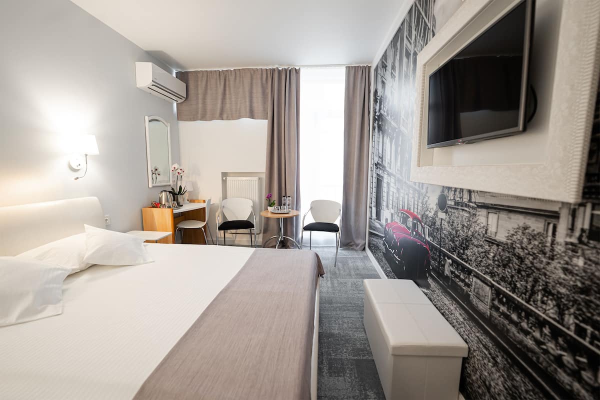 A hotel room with a large bed, a desk, a chair, a small table, and a TV mounted on the wall.