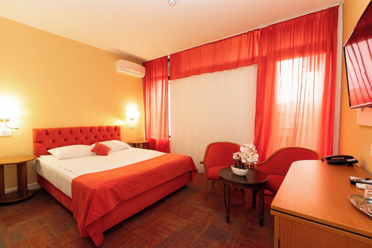 A hotel room with a large bed, a desk, a chair, and a small table with a vase of flowers.