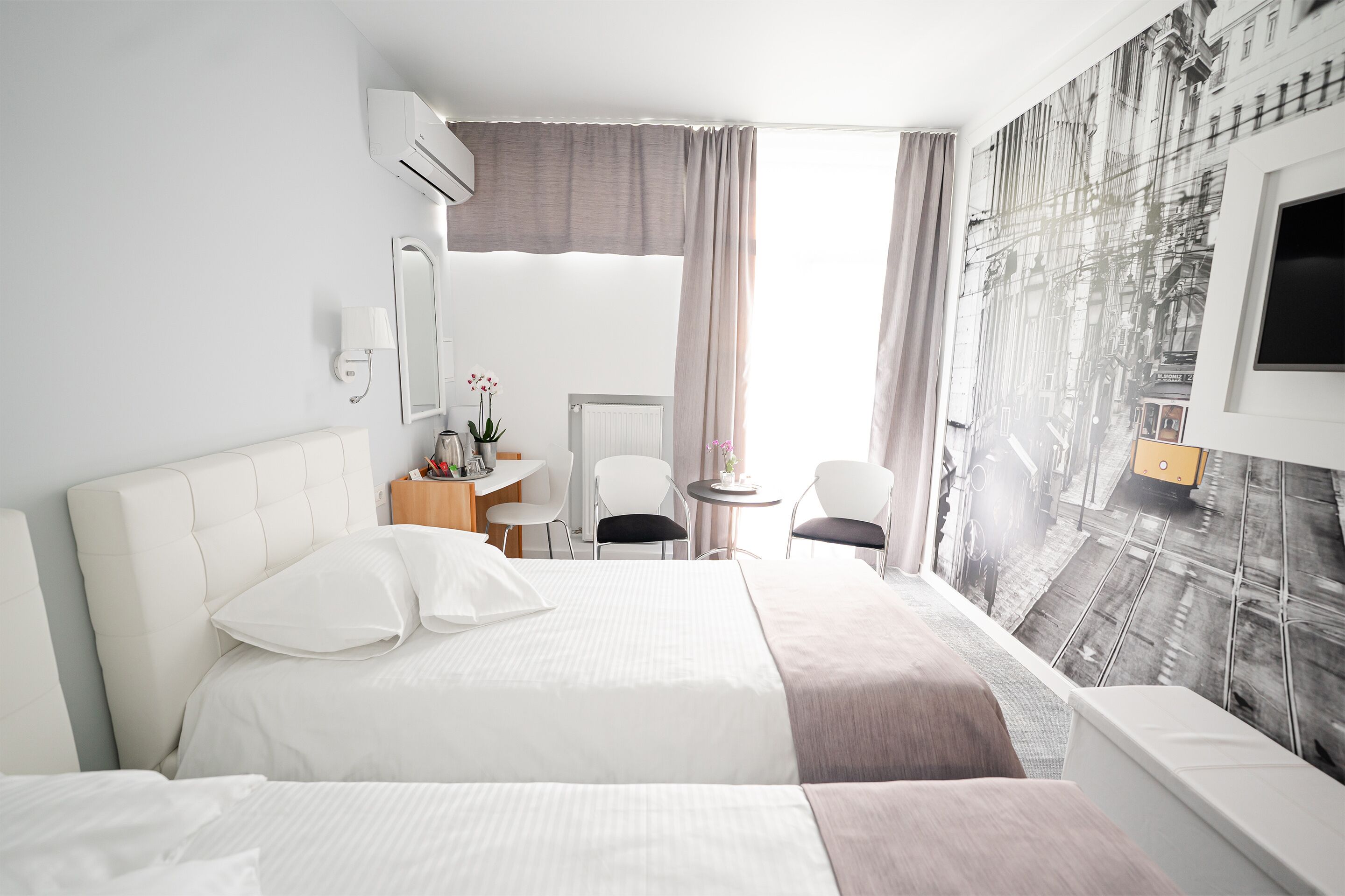 A hotel room with a large bed, a desk, a chair, a small table with a lamp, and a wall-mounted TV.