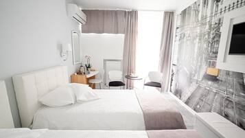 A hotel room with a large bed, a desk, a chair, a small table with a lamp, and a wall-mounted TV.